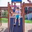 Three children playing on a Space Station castle with a slide in a playground.