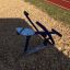Outdoor rowing machine on playground wood chips next to a track.