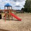 Climbing Booth wooden playground structure with blue roof, red slide, and climbing features in a san