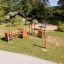 Outdoor playground 'Trixie' with wooden climbing structures and a circular sandbox in a green park.