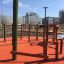Spillikins wooden playhouse on outdoor playground with red safety flooring and surrounding urban bui