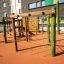 Spillikins wooden playhouse on a modern playground with climbing ropes and wooden structures.