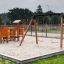 Double Safety Seat double swing on sandy playground with slide and climbing structures.