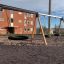 Triple swing with tire seats in playground area in front of brick building.