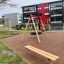 Bench, Steel Construction in a playground with swingset and residential buildings in the background.
