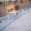 Ryga Bench w/ Backrest placed along a paved pathway in a landscaped area