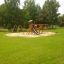 Romping Cottage wooden playground set with slide and swings in a green park