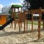 Outdoor playground equipment Romping Cottage with slide, climbing nets, and wooden playhouse.