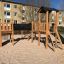 Wooden play set Romping Cottage with slide and climbing net on a sandy playground.