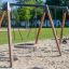 Swing Frame 1(BNS) +1 (double swing) on a sandy playground with a circular seat.