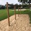 Wooden Rope Bar in a playground with grass and sand surrounding it.