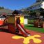 Veranda House single playhouse with slide and adjoining play structures in a playground.