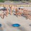 Sonora wooden climbing structure with three blue in-ground trampolines on sandy playground