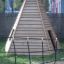 Ural climbing net in front of a wooden pyramid structure in a playground.