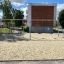 Swing Metal Frame 2+2 (multiple swing) on a sandy playground with trees and buildings in the backgro
