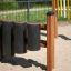 Playground Drums structure with wooden posts and black cylindrical drums on a sandy surface.