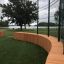 Multiarena Wooden sports facility with curved wooden bench and metal fence in a park setting near a 