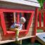 Child playing in Anna's Playhouse wooden playset with red accents.