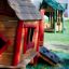 Wooden playhouse for children with red accents from Anna's Playhouse line in a playground setting.