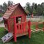 Wooden playground house with red accents and climbing elements from Anna's Playhouse.