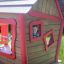 Wooden playhouse with red trim and a smiling child peeking through the window from Anna's Playhouse