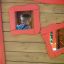 Child looking out from inside wooden Anna's Playhouse with red frames.