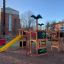 Jungle castle with slide in a playground with other play equipment and buildings in the background.