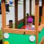Child playing inside a green wooden Bus playground equipment.