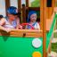 Children play in a wooden Bus structure in a playground.