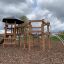 Meru wooden playground structure with climbing nets and a slide.