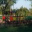 Fortress playhouse with slide in a playground surrounded by trees and green fence.