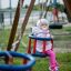 Double Baby Swing with a baby in a pink outfit enjoying the ride on a playground.