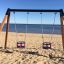 Double Baby Swing set on a sandy beach with a view of the sea.