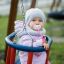 A baby in warm clothes sitting on a Double Swing.