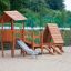 Galapagos wooden playhouse with slide in a sandy playground.