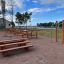 Outdoor fitness equipment and picnic tables in a park near a lake.