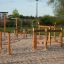 Trim trail wooden playground equipment with ropes and balance beams on sandy ground.
