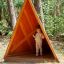 Child standing inside Tipi Nature wooden house on playground in forest setting