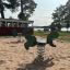 Green Rabbit Rocking spring rider playground equipment on sandy ground with trees and lake in the ba