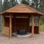 Wooden gazebo shelter with wooden walls in a forest setting.
