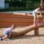 Children playing on the Ramp wooden balance beam in an outdoor playground.