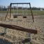 Balance playground equipment including a wooden seesaw and swings in an outdoor sandy area.
