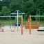 Nature Double Swing on a sandy playground with trees in the background.