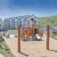 Flexi Seat Single Swing on a sandy playground with residential buildings in the background