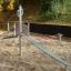 Starfish steel structure playground equipment in a sandy play area with green foliage in the backgro