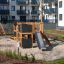 Modern wooden playground set 'Climbing Kiosk Nature' in a residential complex courtyard.