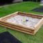Wooden sandbox filled with sand on a grassy lawn.