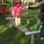 Child balancing on Surf Board playground equipment with parent's support.