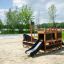Small Ship Nature wooden playground structure with slide on sandy ground in park.