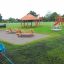 Firehouse playground set with red slide and wooden structures in park.